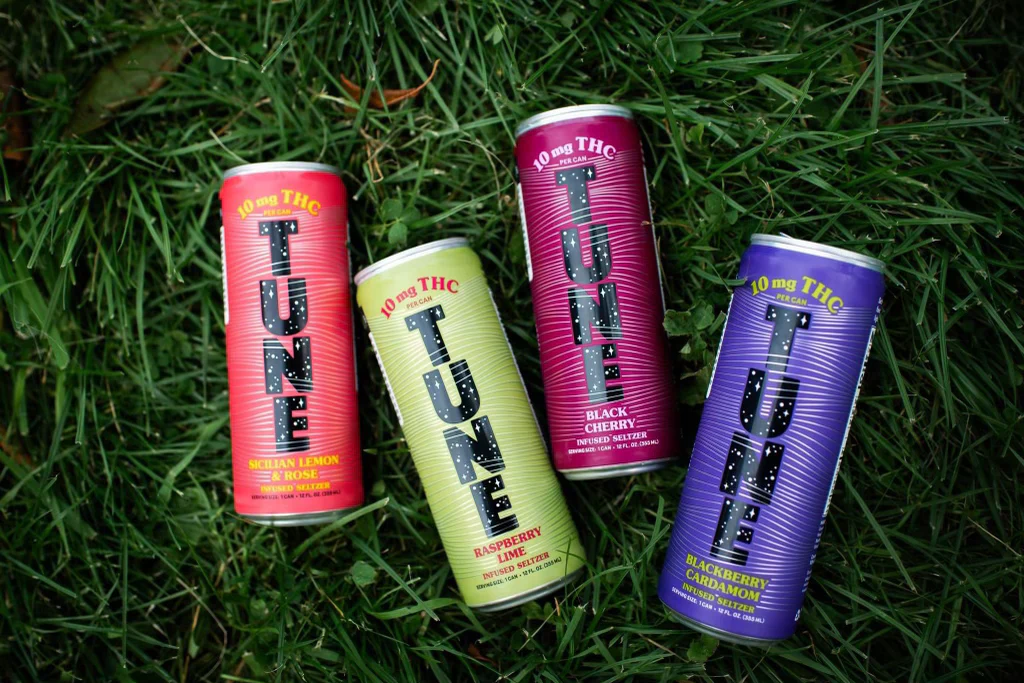 Four colorful cans of Tune infused seltzer placed on green grass