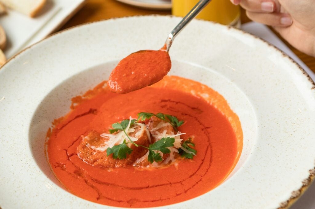 Creamy tomato soup served with herbs and bread on the side